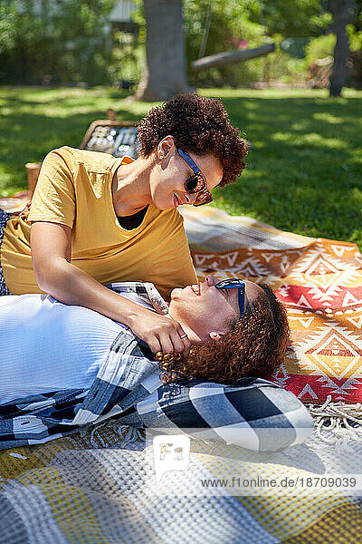 Happy lesbian couple cuddling and talking on picnic blanket in park
