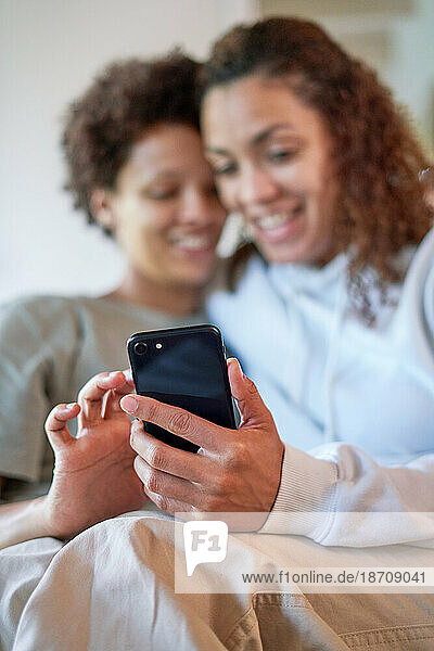 Happy lesbian couple using smart phone together at home