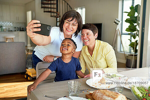 Happy lesbian couple and son taking selfie at dinner table