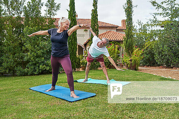 Happy  active senior couple practicing yoga in villa garden