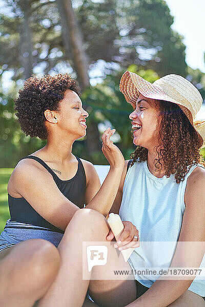 Happy lesbian couple applying sunscreen to face in summer backyard
