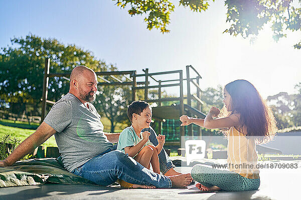 Father and children sitting on trampoline in sunny backyard