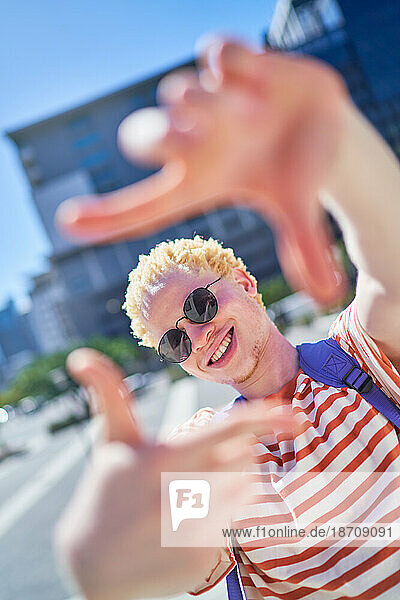 Portrait happy young man gesturing finger frame in sunny city
