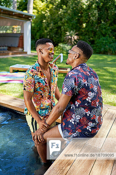 Happy young gay male couple at backyard summer swimming pool