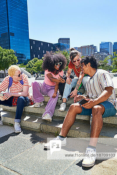 Young friends hanging out  using smart phones in sunny city park