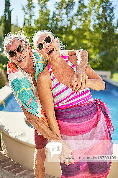 Portrait happy  playful senior couple hugging at sunny poolside