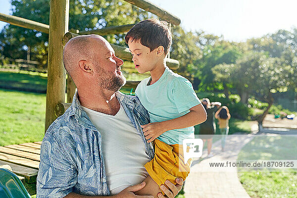 Father holding cute son with Down Syndrome in sunny summer park