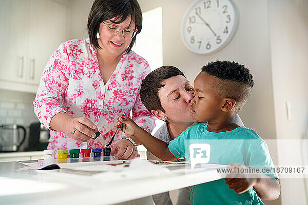 Affectionate lesbian couple kissing son painting in coloring book