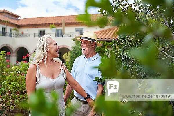Happy senior couple walking in garden outside summer villa