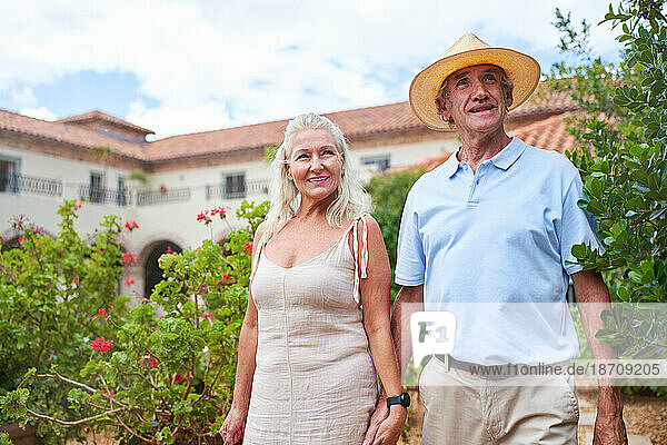 Portrait happy senior couple walking in garden outside villa