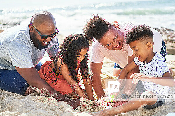 Happy gay male couple with kids playing in sand on sunny beach
