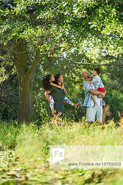 Happy family standing below tree in sunny summer park