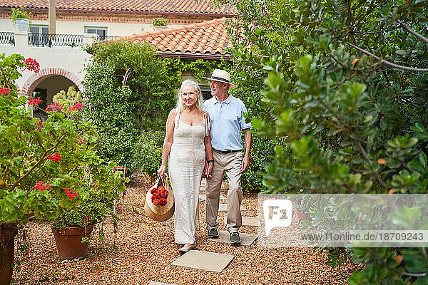 Happy senior couple with flowers walking in garden outside villa