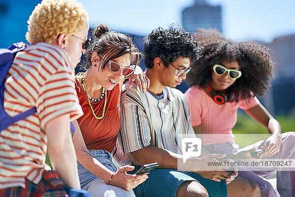 Young friends using smart phones in sunny city