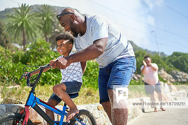Father teaching happy son how to ride a bike on sunny boardwalk