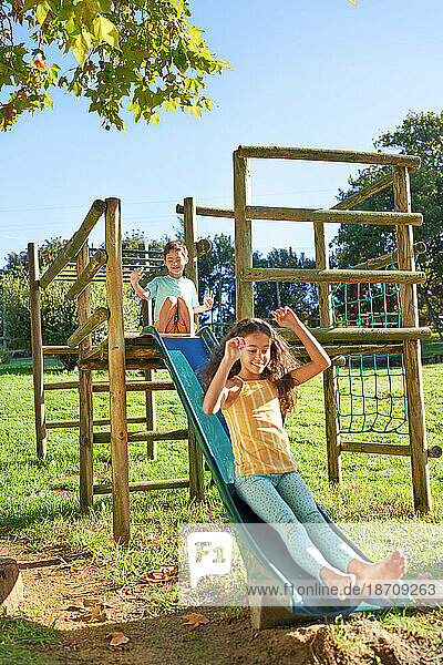 Carefree brother and sister playing on slide at playground structure
