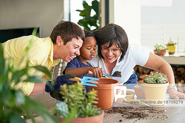 Happy lesbian couple and son planting plants in flowerpots on patio
