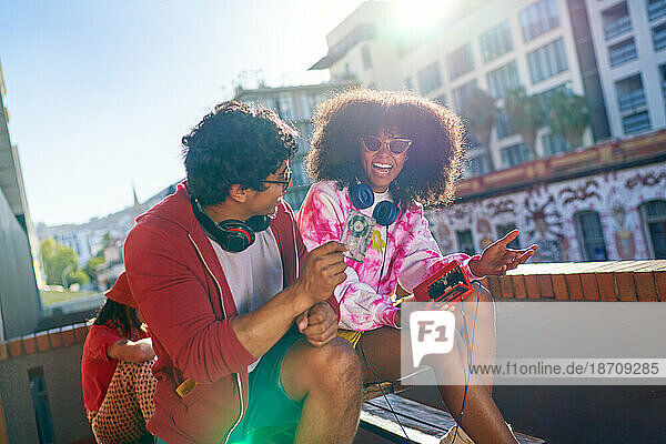 Happy young friends listening to music on sunny urban balcony