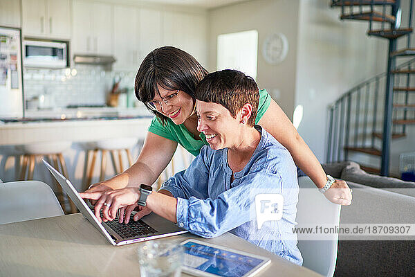 Happy lesbian couple using laptop together in dining room at home