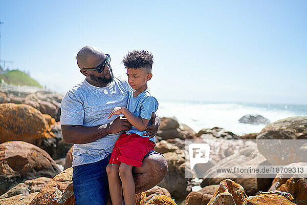 Affectionate father holding son on sunny beach rocks