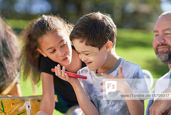 Sister watching brother with Down Syndrome using smart phone in park