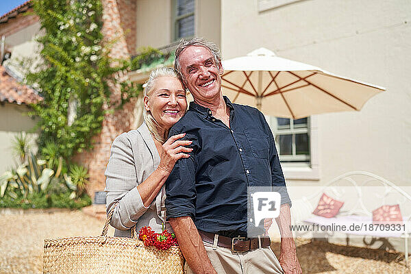 Portrait happy senior couple hugging on sunny summer villa patio