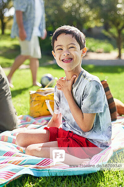 Portrait cute boy with Down Syndrome on picnic blanket in park