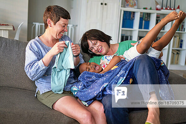 Happy lesbian couple tickling son on living room sofa