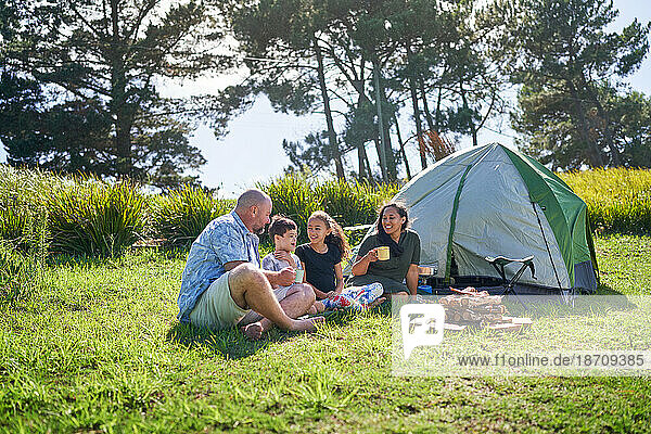 Happy family talking and drinking outside tent at sunny summer campsite