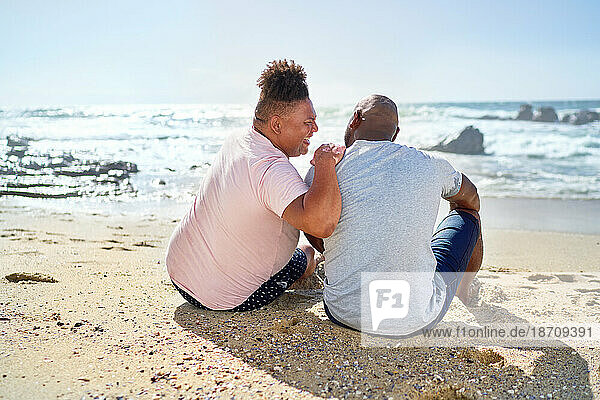 Gay male couple laughing on sunny ocean beach