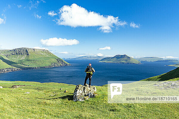 Hiker standing on top of rock contemplating the fjord in summer  Nordradalur  Streymoy Island  Faroe Islands  Denmark  Europe