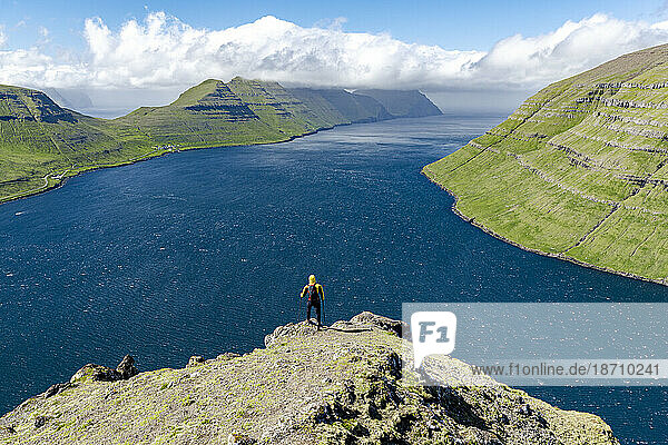 High angle view of hiker admiring mountains and ocean standing on top of a mountain  Klaksvik  Bordoy Island  Faroe Islands  Denmark  Europe