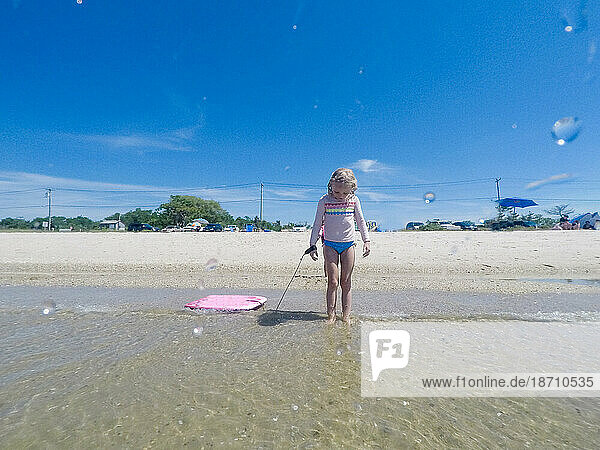 young girl at waters edge wave hitting feet holding boogie board