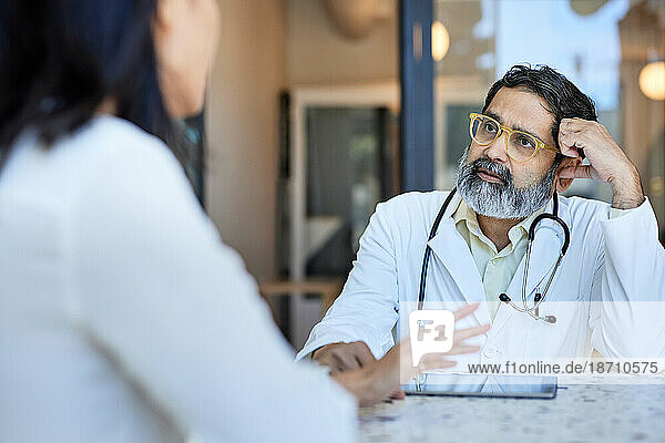 Mature doctor listening to female patient sitting in clinic