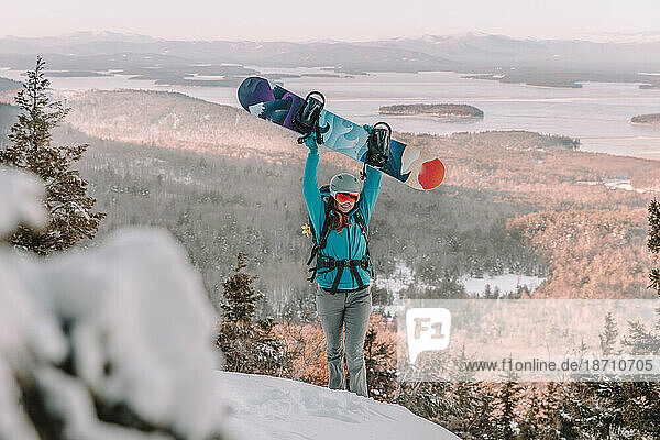 Woman with ski goggles and snowboard on mountain overlooking lake