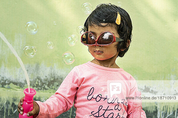 Cute little girl making fun with soap bubbles at outdoors