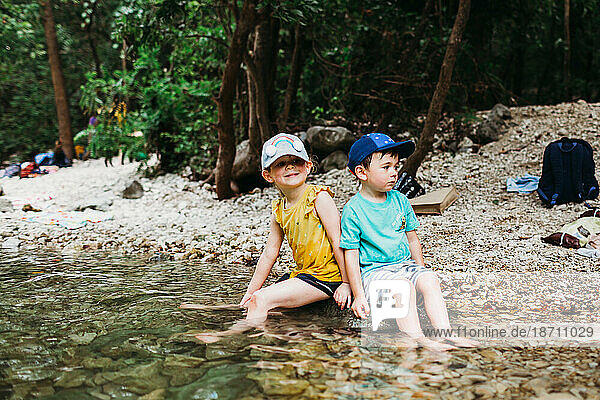 Young girl and boy sitting on rock in water at Barton Springs