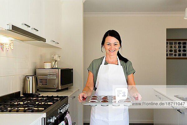 Entrepreneur baker holding a tray of cupcakes next to the oven