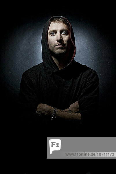 Portrait of young man with a hood  on black backdrop with only his face illuminated  back lit..