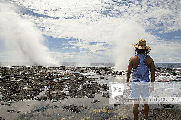 Man wearing blue singlet and shorts  staring at blowholes and ocean