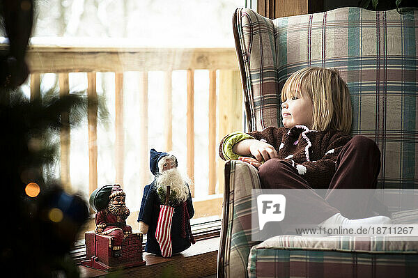A young girl look out a large window as snow falls during Christmas holidays.