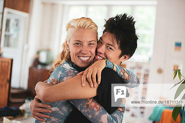 Interracial queer couple hug and laugh happily at home