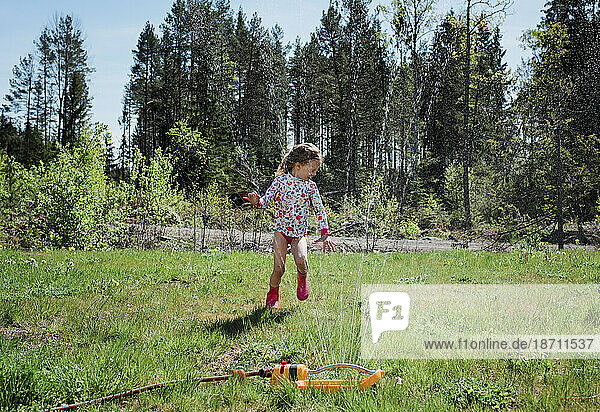 young girl running through a sprinkler in her garden playing