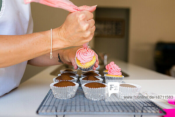 A female's hands decorating cupcakes with pink frosting