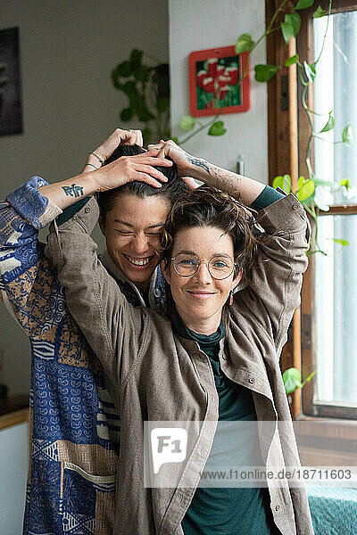 queer female couple playfully hold each other laughing at home