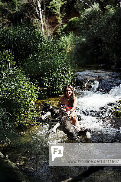 Blond woman bathing in nice river with siberian husky dog.