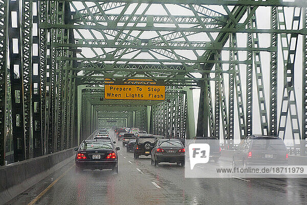 There is rain and heavy traffic on the freeway bridge which separate Oregon and Washington States.