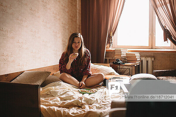 Young woman eating sandwiches in bed at home
