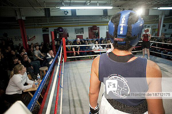 Two female boxers stare each other down during a break in the fight while judges  fans  and coaches watch from ringside  Toronto