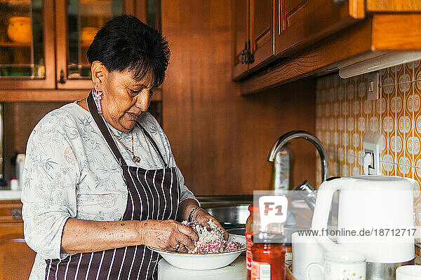 older latin american woman kneading meat cooking in the kitchen